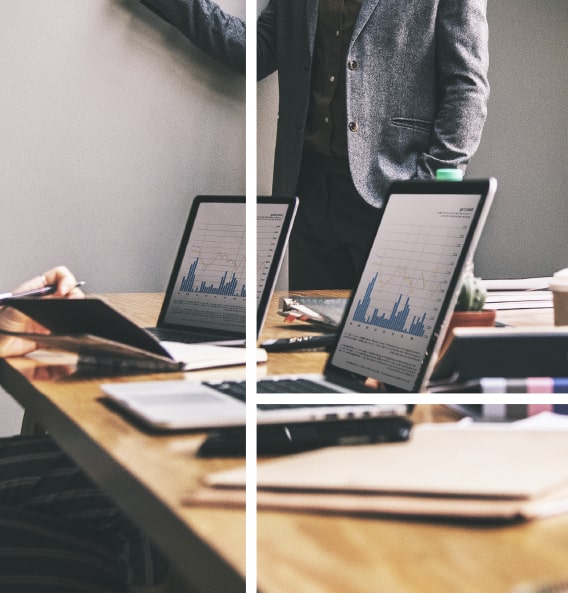 A man in a black coat stands behind a table with two open laptops displaying an analytics diagram